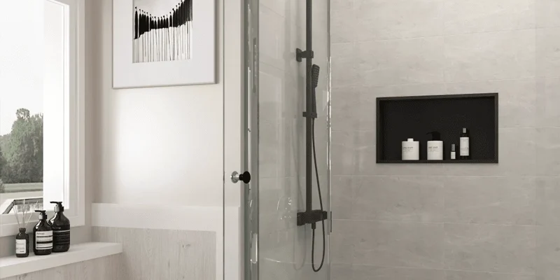 A quartz shower niche creates built-in storage without introducing a projecting caddy or a collection of small tiled edges into the shower. It may be fabricated as a complete quartz-lined opening, a solid bottom ledge, an internal shelf, or a combination of quartz pieces coordinated with the surrounding wall tile. The finished appearance can be simple, but the detail requires early planning. Shelf height, usable depth, exposed edges, vein direction, joint locations and the underlying shower assembly all affect the result. Decisions made after the wall has already been framed and waterproofed may limit the available layout or require additional joints. This guide explains how quartz shower niches are designed and fabricated, what should be confirmed before production, and how the stone fabricator’s work connects with the framing, waterproofing and tile stages of a bathroom project. Explore Custom Stone Shower Boxes Browse Quartz Surfaces Quick answer: Quartz can provide a smooth, coordinated surface for shower niche ledges, shelves and wall linings. The best result depends on selecting a quartz product suitable for the intended interior wet-area application, supporting each piece correctly and coordinating the fabrication with the shower’s separate waterproofing system. Quartz is the visible finish; it is not a substitute for the membrane and properly prepared substrate behind it. Table of Contents What Is a Quartz Shower Niche? Is Quartz Suitable for a Shower Niche? Choosing the Right Quartz Niche Shelf Layout Quartz Edge Profiles for Shower Niches Vein Direction, Joints and Pattern Layout How a Custom Quartz Shower Niche Is Fabricated Quartz Shower Niche Planning Checklist Quartz Shower Niche FAQs What Is a Quartz Shower Niche? A quartz shower niche is a recessed storage opening that uses fabricated quartz for one or more of its visible surfaces. Although the terms quartz niche, stone shower box and recessed shower shelf are sometimes used interchangeably, they can describe several different construction details. Some niches are lined entirely with quartz. Others retain tile on the back and side walls but use a solid quartz piece for the bottom ledge or shelf. The appropriate option depends on the wall construction, desired appearance, available slab material and the number of exposed edges that must be finished. Full Quartz-Lined Shower Niches In a fully lined niche, fabricated quartz pieces cover the back, sides, top and bottom of the recessed opening. This creates a consistent surface with fewer visible grout lines than a niche finished entirely with small tile pieces. A full quartz lining can work well when the niche is intended to coordinate with a quartz vanity, shower jamb or another bathroom surface. It also allows the fabricator to control exposed edges and colour transitions more carefully. However, a full lining is not automatically joint-free. Most custom niches require separate pieces to fit within the opening and allow practical installation. Joint placement, inside corners and installation tolerances should therefore be resolved before fabrication rather than concealed in a last-minute site decision. Quartz Shelves and Sills in Tiled Niches A tiled niche can use quartz selectively at the locations that benefit most from a solid piece. Common examples include: A quartz bottom sill: provides one continuous ledge beneath the bottles and toiletries. An internal quartz shelf: divides a taller niche into two usable storage levels. Quartz side and top returns: create finished edges while retaining a tile or feature panel at the back. A quartz frame: visually outlines the opening and coordinates it with other fabricated bathroom details. This mixed-material approach can reduce the amount of quartz required while keeping the most visible horizontal surfaces smooth and coordinated. It also allows a feature tile at the back of the niche to remain part of the overall shower design. Quartz may be used throughout the niche or selectively for the bottom ledge, internal shelf and exposed returns. Custom-Fabricated vs. Prefabricated Quartz Niches A prefabricated niche has a predetermined outside and inside size. It can simplify the wall preparation stage, but its shelf positions, proportions, colour and edge details may offer limited customization. A custom-fabricated quartz niche is made around project-specific dimensions. It can be coordinated with the height of shampoo bottles, the tile module, the location of wall studs and the pattern of other quartz surfaces in the bathroom. Custom fabrication also makes it possible to use slab remnants when the available piece has the correct colour, thickness and usable dimensions. The critical distinction is that the fabricated quartz and the recessed waterproof enclosure are not necessarily the same component. A waterproofed niche or prepared wall cavity may be completed first, after which quartz pieces are measured, fabricated and installed as the visible finish. The project team should confirm the sequence before final measurements are taken. Is Quartz Suitable for a Shower Niche? Quartz can be a practical option for a shower niche, particularly when a smooth appearance, consistent pattern and limited surface absorption are priorities. Engineered quartz is commonly used for interior bathroom surfaces, and certain manufacturers also identify their products for applications such as shower surrounds, wall cladding, recessed shelving or bathroom shelves. That does not mean every quartz colour, finish, thickness or brand should automatically be specified for every shower detail. Product documentation, fabrication requirements and warranty conditions should be reviewed for the exact material being considered. Where Quartz Performs Well A suitable quartz product can offer several advantages inside a properly constructed shower niche: Consistent colour and pattern: useful when coordinating the niche with a vanity countertop or other fabricated components. Smooth, easy-to-wipe surfaces: particularly helpful on shelves that collect soap residue and water droplets. Fabricated edge options: exposed ledges and returns can be cut and finished before arriving at the installation site. Low routine maintenance: engineered quartz generally does not require the periodic sealing associated with many natural stones. Custom sizing: shelves and lining pieces can be produced for the measured opening rather than forcing the design around a stock accessory. These advantages relate to the quartz finish itself. Corners, perimeter joints, supports and transitions still require appropriate installation materials and workmanship. What Quartz Does Not Replace Quartz should not be described as the waterproofing system for the shower wall. Water management takes place behind the visible finish through the properly prepared substrate, membrane, niche enclosure and sealed transitions to the surrounding shower assembly. This distinction matters because a smooth quartz surface may still have joints around its perimeter and where separate pieces meet. If water reaches those joints, the assembly behind the quartz must already be designed to manage moisture safely. The stone fabricator should coordinate with the contractor responsible for framing, wall preparation, waterproofing and tile installation. Responsibilities should be clear before fabrication so that quartz pieces are not used to conceal an incomplete or incompatible substrate. Confirming Product and Finish Suitability Before approving a quartz slab for a shower niche, confirm: Whether the specific manufacturer permits the proposed interior wet-area application Whether the selected finish is appropriate for frequent exposure to water and bathroom cleaning products Which adhesives and sealants are compatible with both the quartz and waterproofing system Whether the selected thickness can be supported at shelves and projecting edges How cut edges, corners and the underside of shelves will be finished Whether the warranty requires fabrication or installation by an approved professional Planning note: Choose the exact quartz product before finalizing the niche dimensions. Slab thickness, pattern scale, available remnant size and edge treatment can all affect the usable interior space and final appearance.