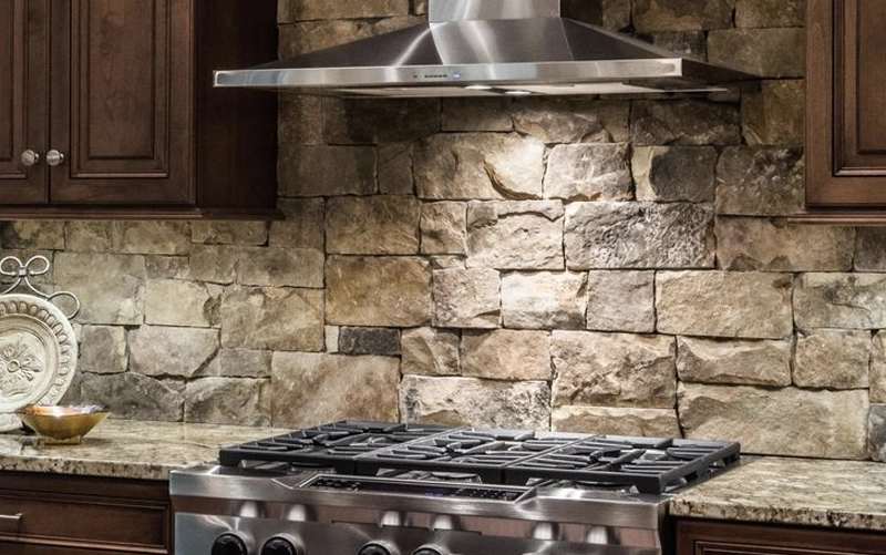Full-height stone slab backsplash installed behind a kitchen range and wall-mounted hood