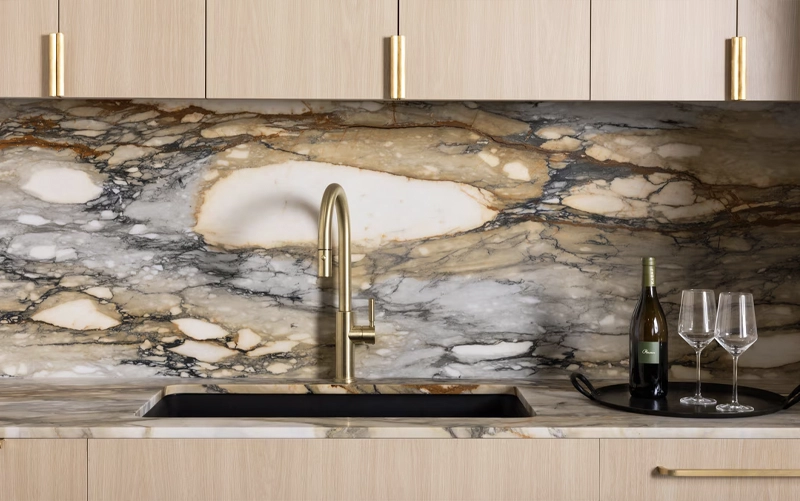 Kitchen stone backsplash being cleaned carefully around a range and countertop joint